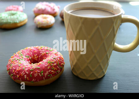 Glass Cup of hot coffee on a black table surrounded by colorful donuts Stock Photo