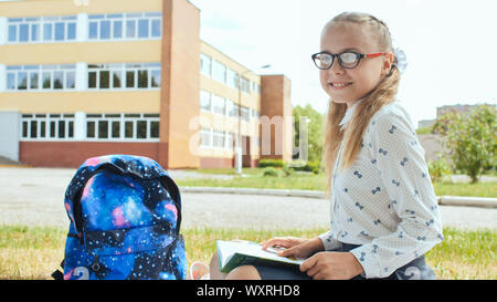 Porter of an 11 year old schoolgirl girl sitting on the background of her school. Stock Photo