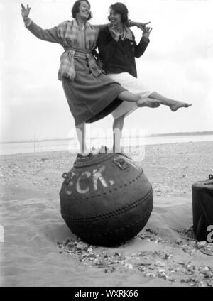 AJAXNETPHOTO. 1920-30S (APPROX). LOCATION UNKNOWN, ENGLAND. - SEASIDE SNAPSHOT - TWO YOUNG LADIES POSE FOR THE CAMERA STANDING ON A WRECK BUOY ON A BEACH. PHOTOGRAPHER:UNKNOWN © DIGITAL IMAGE COPYRIGHT AJAX VINTAGE PICTURE LIBRARY SOURCE: AJAX VINTAGE PICTURE LIBRARY COLLECTION REF:()AVL PEO 182303 0474 Stock Photo