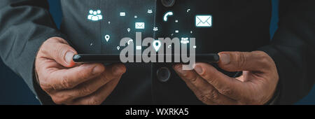 Businessman holding digital tablet in his hands with white glowing contact, communication and location icons coming out of it in a conceptual image. Stock Photo