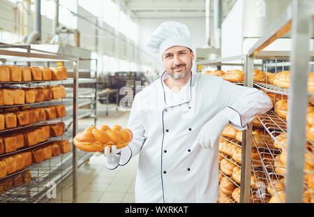 A baker in a bakery against the shelves of bread. Stock Photo