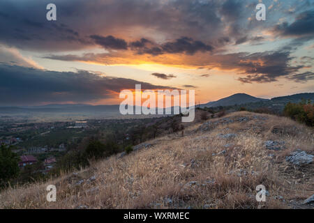 Beautiful view from a hill covered by dry grass and rocks on an epic sunset colors of the sky and distant hospital and village Stock Photo