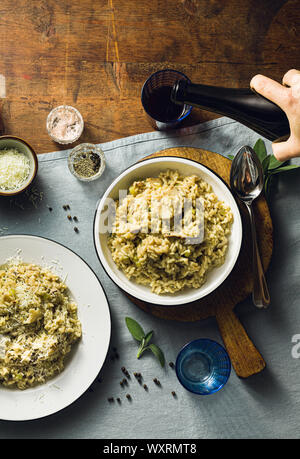 Classic Italian risotto with mushrooms on a wooden table with a blue linen tablecloth. red wine. bottle and glasses. top shots, male hand pours wine Stock Photo
