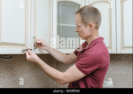 Installation of kitchen furniture. The man is putting handles to door cabinets. Stock Photo