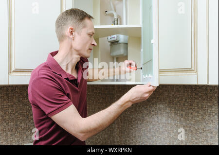 Installation of kitchen furniture. The man is using a screwdriver to adjust the door of the cabinet. Stock Photo