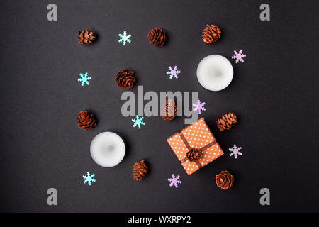 Top view flat lay christmas geometry composition of pine cones, candles, fake snowflakes and small gift box on black background
