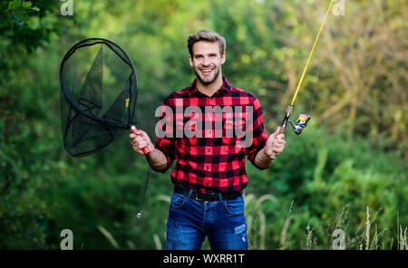 Fishing day. Handsome guy in checkered shirt with fishing equipment nature  background. Fishing in my hobby. Summer weekend concept. Hipster fisherman  with rod spinning net. Hope for nice fishing Stock Photo 