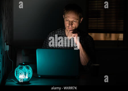 The man at work in the night is looking into a laptop screen. Stock Photo