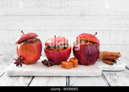 Baked apples with caramel, brown sugar and and nuts. Serving board on a white wood background. Homemade autumn dessert. Stock Photo