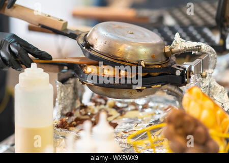 Chef checking toasting burgers in crusty white buns packed in a griddle on a catering table at a street market or event in a close up view Stock Photo