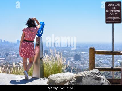 Lady leaning on telescope in Hollywood hills with Los Angeles skyline in the distance