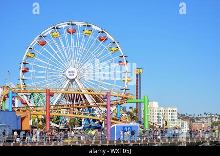 Santa Monica ferris wheel on the pier with other fairground rides and a large crowd Stock Photo