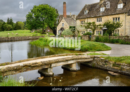 Yellow Cotswold limestone footbridge over the River Eye in Lower Slaughter village in Cheltenham England with The Old Mill museum buildings