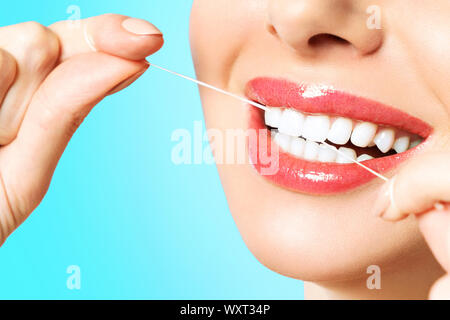 Young beautiful woman is engaged in cleaning teeth. Beautiful smile healthy white teeth. A girl holds a dental floss. The concept of oral hygiene. Stock Photo