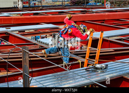 Cypress, CA / USA - Sept. 16, 2019: Construction worker in hardhat balances precariously high up on the scaffolding of a building site. Stock Photo