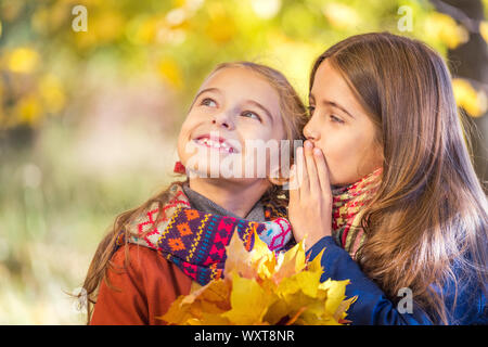 Two cute smiling 8 years old girls chatting in a park on a sunny autumn day. Stock Photo