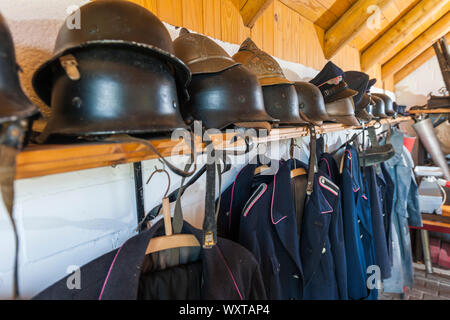 Perspective view along strung old fire department uniforms of different eras with focus on historical helm on the shelf. Stock Photo