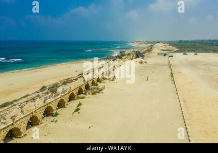 Ruins of the Roman aqueduct arches on the beach of Caesarea Israel with blue see and sky Stock Photo