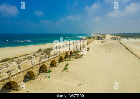 Ruins of the Roman aqueduct arches on the beach of Caesarea Israel with blue see and sky Stock Photo