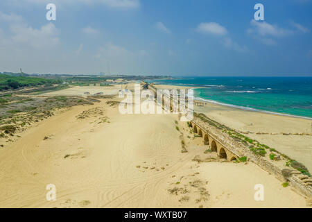 Ruins of the Roman aqueduct arches on the beach of Caesarea Israel with blue see and sky Stock Photo