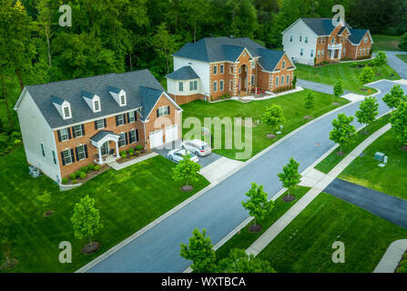 American luxury real estate single family houses with brick facade and two car garages in a new construction Maryland street neighborhood USA aerial Stock Photo