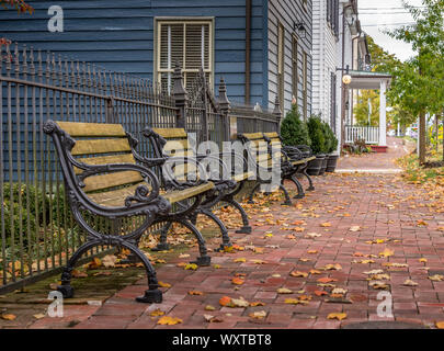 Wooden bench with iron frames on a colonial brick street in New Market Maryland with autumn leaves Stock Photo