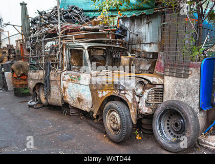 Wrecked pickup truck with pieces of used spare parts on its top, left abandoned along alleyway. Stock Photo