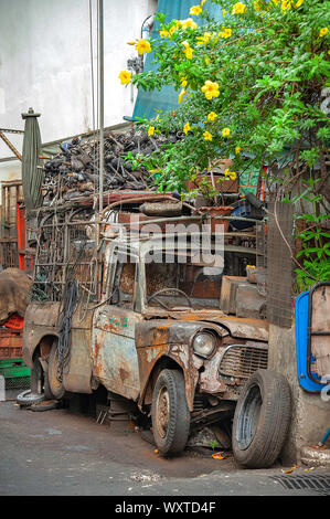 Wrecked pickup truck with pieces of used spare parts on its top, left abandoned along alleyway. Stock Photo