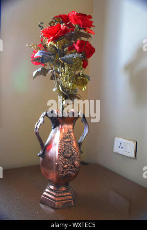 rose made of plastic and golden leaves in a plastic jug with gray background Stock Photo