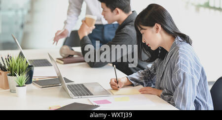 Young adorable businesswoman working on her project with her team members discussing in the background Stock Photo