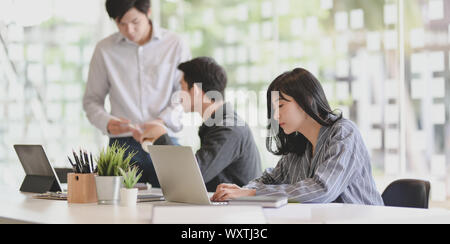 Young adorable businesswoman working on her project with her team members discussing in the background Stock Photo