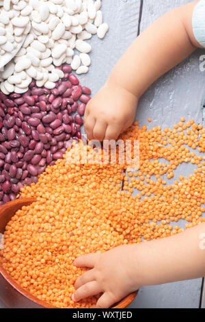 Kids hands holding red beans and lentils on wooden table Stock Photo