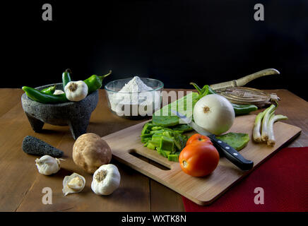 Mexiccan still life with onions nopales chili or chiles potatoe tomato garlic and a molcajete with a bowl with flour and a tortilla maker on a rustic Stock Photo