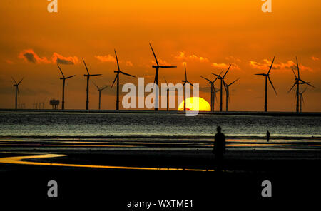 The sun sets behind Burbo Bank wind farm and 'Another Place', an art installation by Anthony Gormley, at Crosby Beach on Merseyside in north west England. Stock Photo