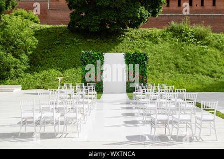 Beautiful setting for outdoors wedding ceremony waiting for bride and groom and guests. Wooden chairs decorated with flowers, are in the zone of the Stock Photo