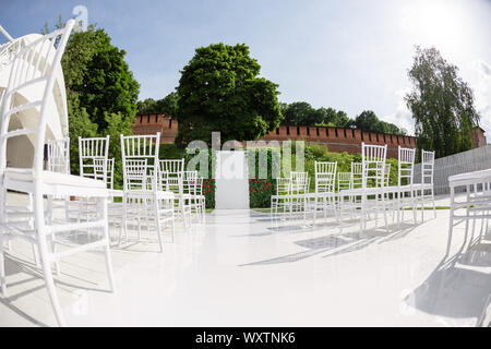 Rows of empty white chairs sitting on a wooden floor. Wedding chairs with flowers at ceremony outdoors Stock Photo