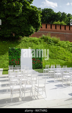 Rows of empty white chairs sitting on a wooden floor. Wedding chairs with flowers at ceremony outdoors Stock Photo