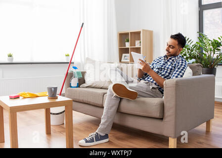 household and time management concept - indian man making to do list in notebook after home cleaning Stock Photo