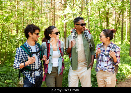 travel, tourism, hike and people concept - group of friends with backpacks talking in forest Stock Photo
