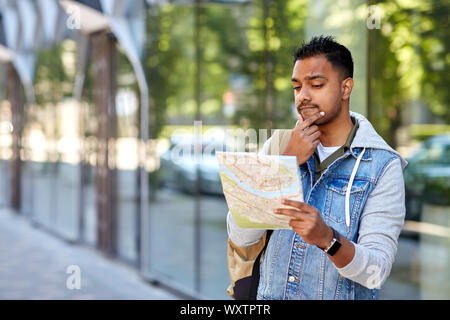 travel, tourism and backpacking concept - indian man traveling with backpack and map in city searching location Stock Photo