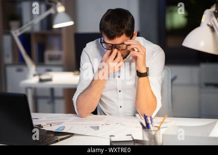 business, deadline and stress concept - tired businessman in eyeglasses working at night office Stock Photo