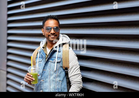 travel, tourism and lifestyle concept - smiling indian man with backpack drinking smoothie from plastic cup with straw on city street Stock Photo