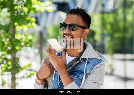 travel, tourism and lifestyle concept - smiling indian man with backpack using voice command recorder on smartphone on city street Stock Photo