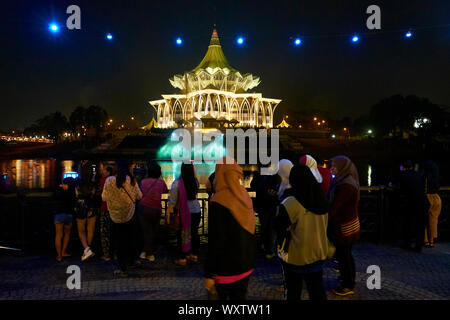 People gather at night to watch the water fountain and laser light show in front of the Legislative Sarawak State Assembly building.  In Kuching, Sara Stock Photo