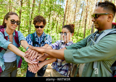 travel, tourism, hike and friendship concept - group of friends with backpacks stacking hands in forest Stock Photo