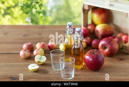 fruits, food and harvest concept - two glasses and bottles of apple juice or cider on wooden table over green natural background Stock Photo
