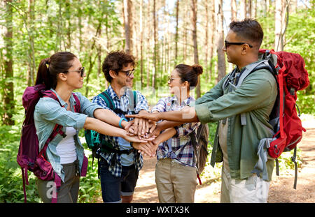 travel, tourism, hike and friendship concept - group of friends with backpacks stacking hands in forest Stock Photo