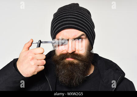 Barber, hipster barbershop assistant with great beard holds razor near eye. Stock Photo