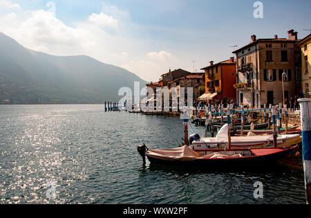 Colorful and picturesque houses at Montisola, Lake Iseo, Lombardy Italy with moored boats and waterfront promenade on a misty day Stock Photo