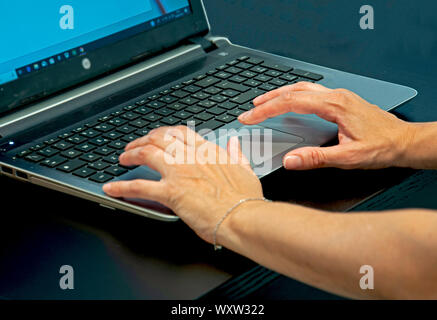 A close up of a womans hands typing on a laptop keyboard on a black desk. Stock Photo